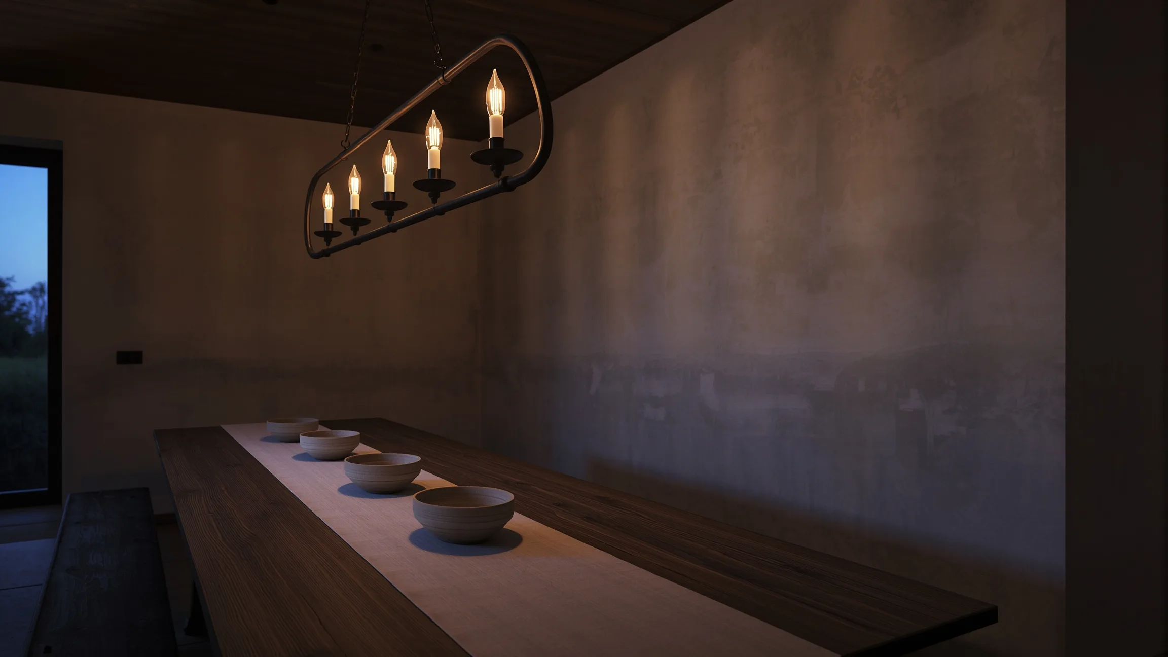 Five-light black candle-style chandelier lit warm over a wood harvest table in a farmhouse dining room at dusk