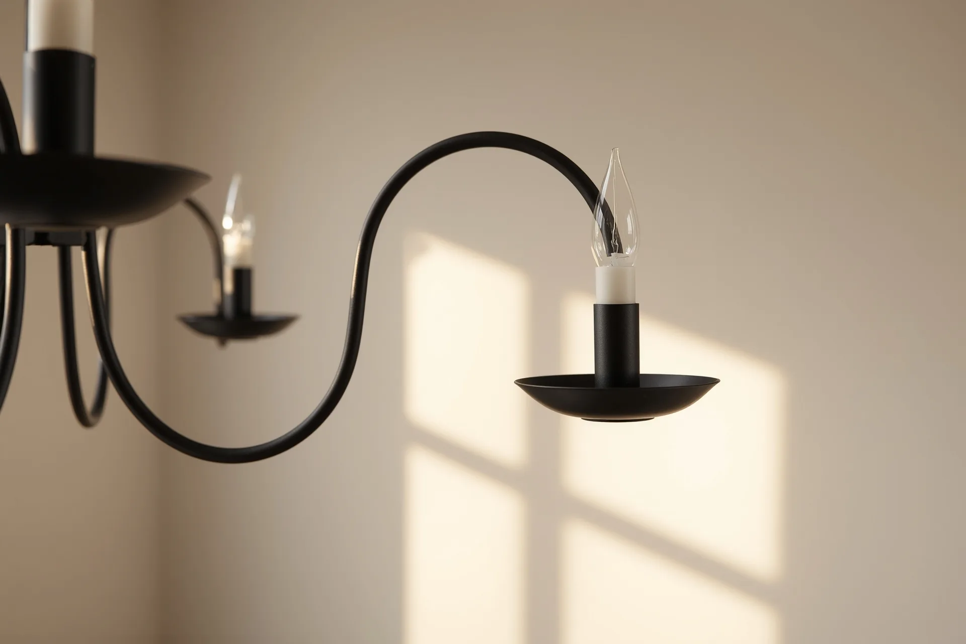 Powder-coated matte black sconce cup sitting straight on its iron arm, matched chain and canopy hardware soft behind